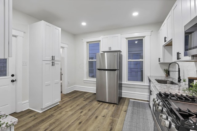 kitchen with light stone countertops, dark hardwood / wood-style flooring, stainless steel appliances, sink, and white cabinetry