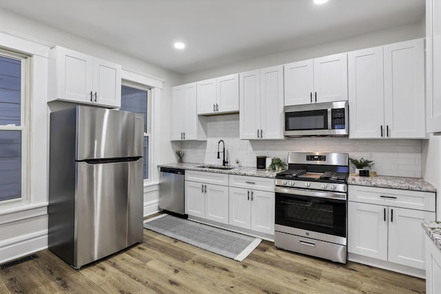 kitchen featuring appliances with stainless steel finishes, light stone counters, sink, wood-type flooring, and white cabinetry