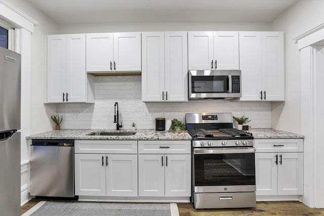 kitchen featuring white cabinets, sink, decorative backsplash, appliances with stainless steel finishes, and light stone counters