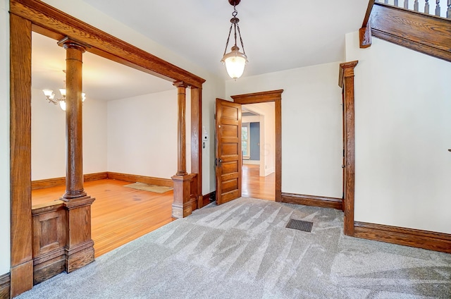 empty room with an inviting chandelier, wood-type flooring, and decorative columns