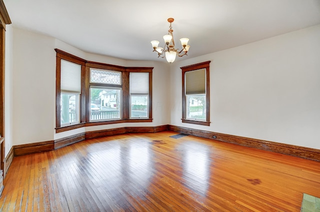 empty room with a chandelier, light wood-type flooring, and a healthy amount of sunlight