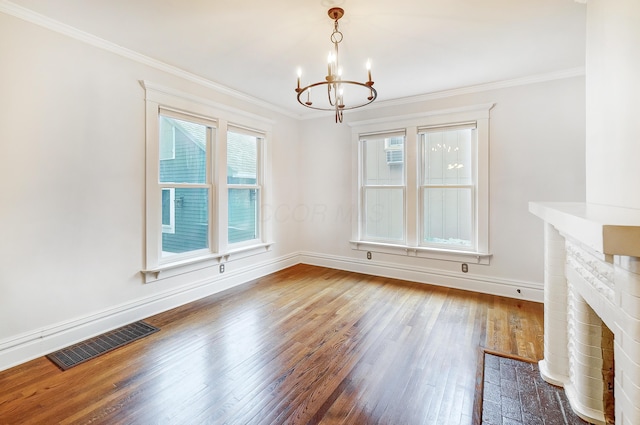 unfurnished dining area featuring a chandelier, crown molding, wood-type flooring, and a brick fireplace