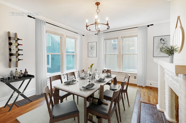 dining room with a chandelier, a fireplace, wood-type flooring, and ornamental molding