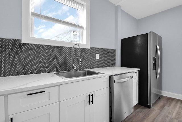 kitchen with appliances with stainless steel finishes, light stone counters, sink, white cabinets, and light hardwood / wood-style floors