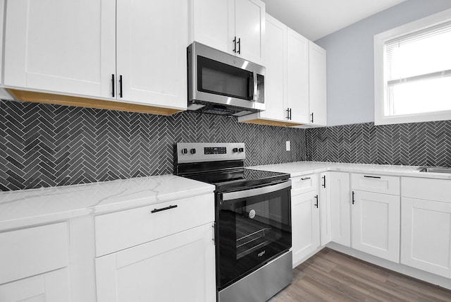 kitchen with white cabinets, light hardwood / wood-style flooring, decorative backsplash, light stone countertops, and stainless steel appliances