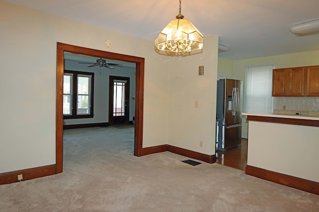 unfurnished dining area with ceiling fan with notable chandelier and light carpet