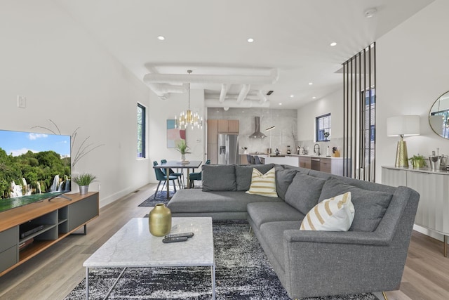 living room featuring beam ceiling, light hardwood / wood-style floors, an inviting chandelier, and sink