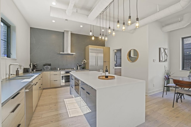 kitchen with sink, a kitchen island, wall chimney range hood, and light hardwood / wood-style flooring