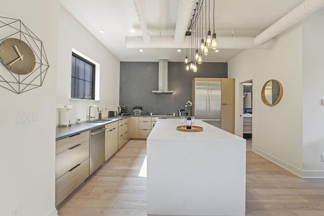 kitchen with wall chimney exhaust hood, stainless steel appliances, a kitchen island with sink, light hardwood / wood-style flooring, and hanging light fixtures