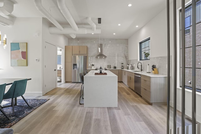 kitchen featuring a kitchen island, stainless steel appliances, wall chimney range hood, and light hardwood / wood-style floors