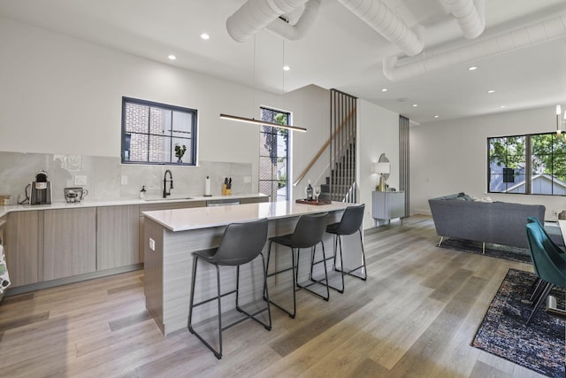 kitchen with sink, a spacious island, light hardwood / wood-style floors, a breakfast bar area, and decorative backsplash