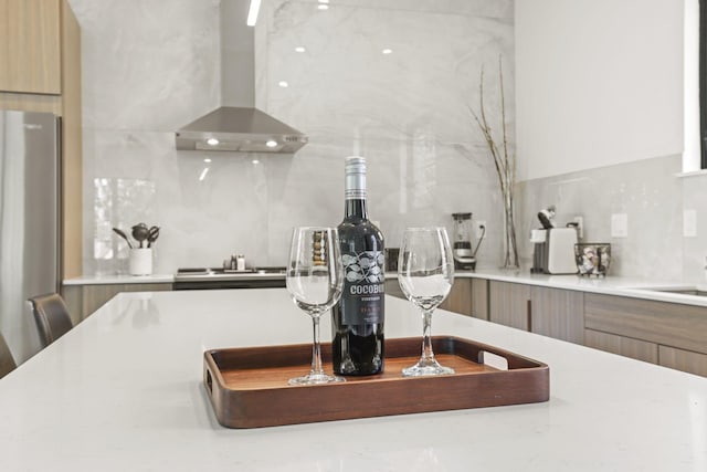 details with decorative backsplash, stainless steel fridge, and wall chimney exhaust hood