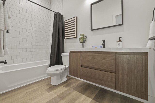 full bathroom featuring hardwood / wood-style floors, vanity, shower / bath combination with curtain, and toilet