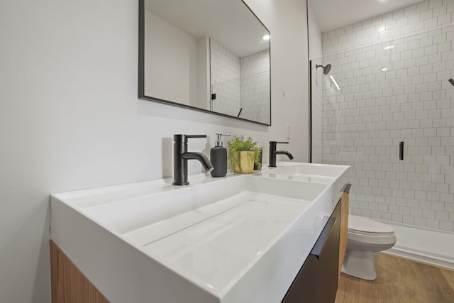 bathroom featuring vanity, toilet, wood-type flooring, and tiled shower