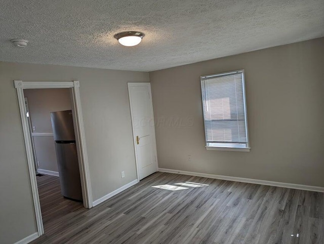 unfurnished bedroom featuring hardwood / wood-style floors, stainless steel fridge, and a textured ceiling