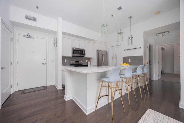 kitchen with white cabinetry, hanging light fixtures, appliances with stainless steel finishes, a kitchen breakfast bar, and dark hardwood / wood-style flooring