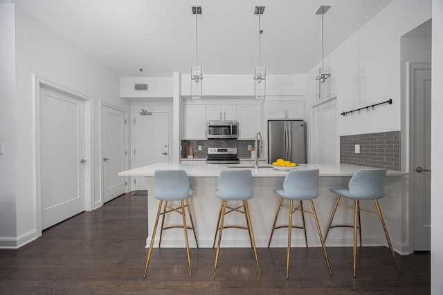 kitchen with sink, appliances with stainless steel finishes, hanging light fixtures, a kitchen breakfast bar, and white cabinets