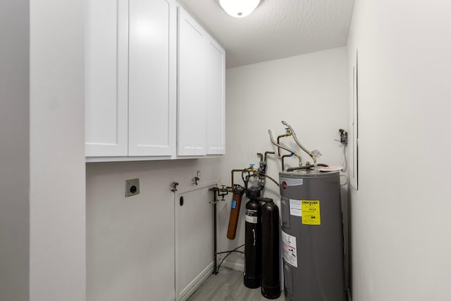 interior space with electric dryer hookup, cabinets, electric water heater, light hardwood / wood-style flooring, and a textured ceiling