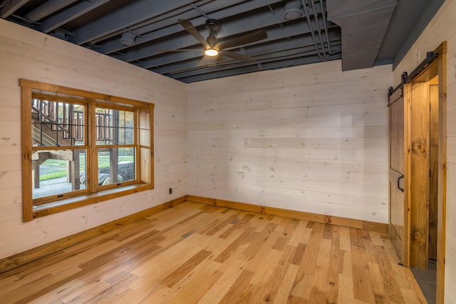 unfurnished room featuring ceiling fan, a barn door, light wood-type flooring, and wooden walls