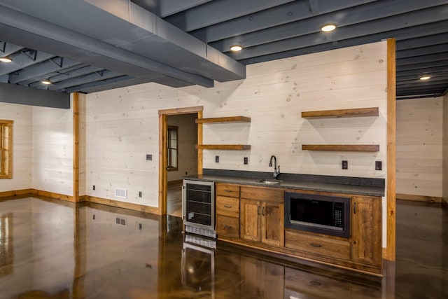 kitchen featuring wine cooler, stainless steel microwave, wooden walls, and sink