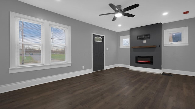 unfurnished living room with plenty of natural light, a fireplace, dark wood-type flooring, and ceiling fan