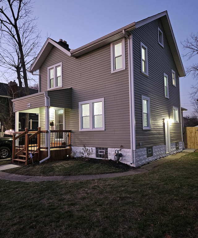 back house at dusk featuring a lawn and a porch