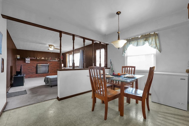 dining space featuring ceiling fan, wood walls, and a brick fireplace