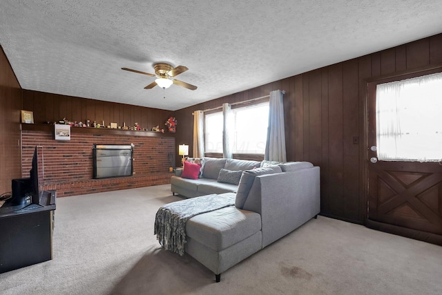 carpeted living room with ceiling fan, a textured ceiling, wooden walls, and a brick fireplace