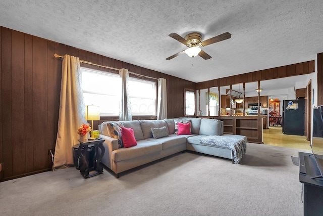 carpeted living room featuring a textured ceiling, ceiling fan, and wooden walls