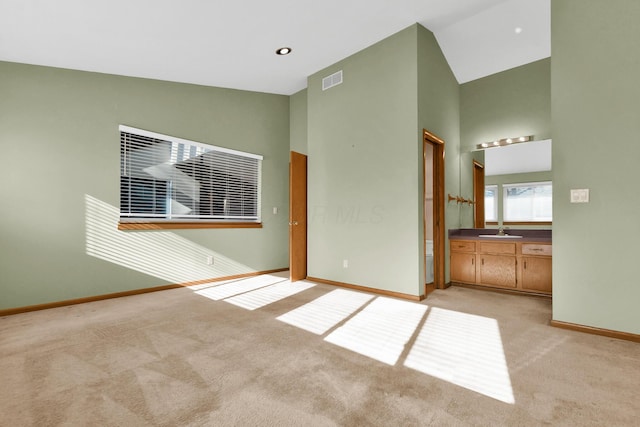 unfurnished bedroom with high vaulted ceiling, light colored carpet, ensuite bath, and sink