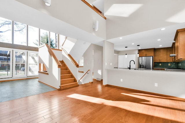 kitchen featuring stainless steel refrigerator with ice dispenser, backsplash, sink, a high ceiling, and light hardwood / wood-style floors