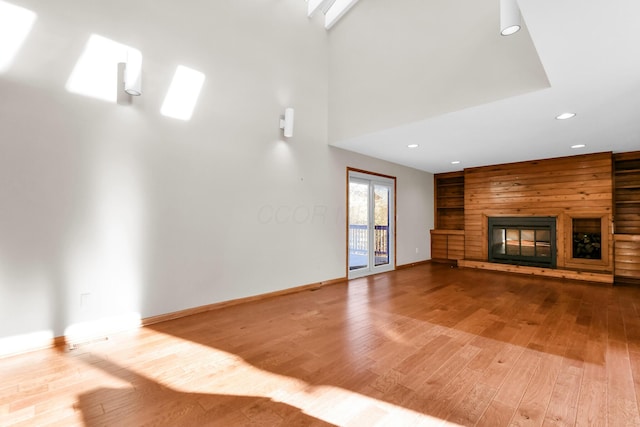 unfurnished living room with a fireplace, wood-type flooring, a towering ceiling, and wooden walls