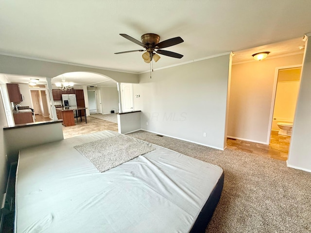 carpeted bedroom featuring ensuite bath, stainless steel fridge, crown molding, and ceiling fan with notable chandelier