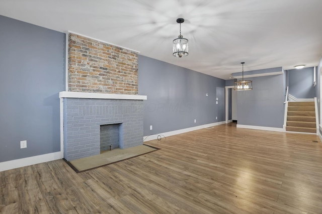 unfurnished living room featuring a fireplace, wood-type flooring, and a notable chandelier