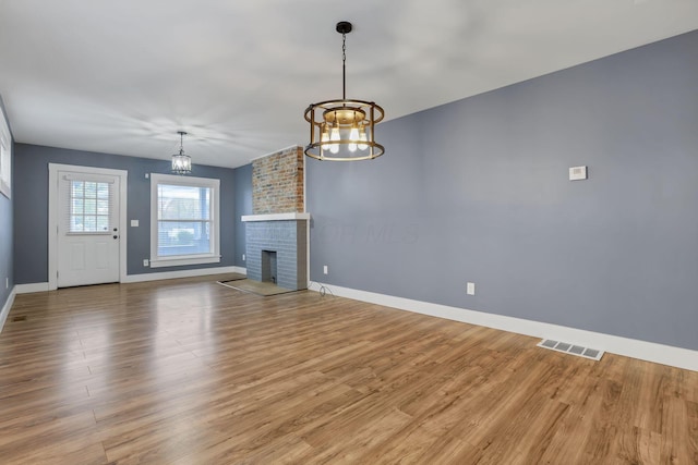 unfurnished living room featuring a fireplace, light hardwood / wood-style flooring, and an inviting chandelier