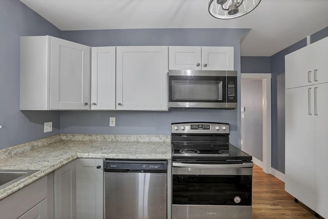 kitchen with white cabinets, light stone countertops, dark wood-type flooring, and appliances with stainless steel finishes