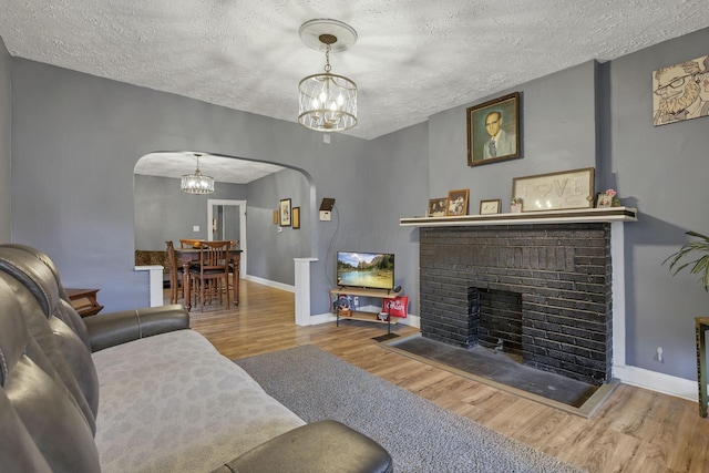 living room featuring a fireplace, hardwood / wood-style floors, a textured ceiling, and an inviting chandelier