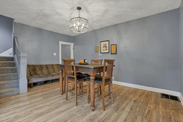 dining room with light wood-type flooring, a textured ceiling, and a chandelier