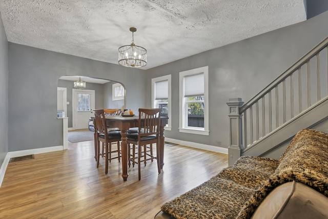 dining space featuring light wood-type flooring, a textured ceiling, and an inviting chandelier