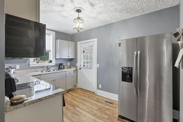 kitchen with pendant lighting, sink, stainless steel refrigerator with ice dispenser, light wood-type flooring, and a textured ceiling