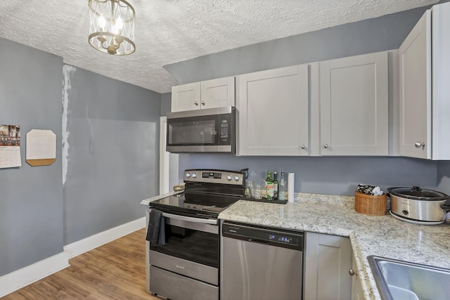 kitchen with white cabinets, a textured ceiling, appliances with stainless steel finishes, light hardwood / wood-style floors, and a chandelier