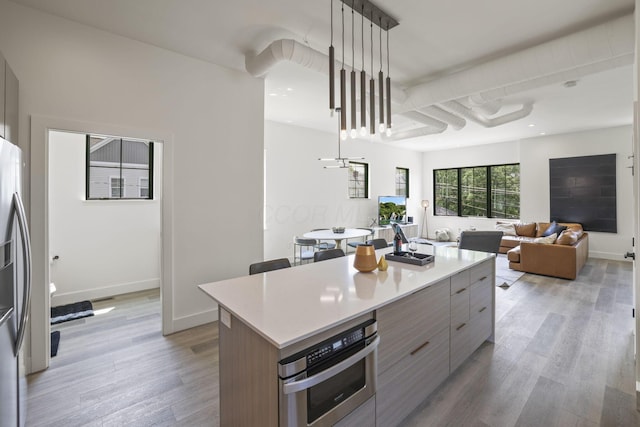 kitchen with light hardwood / wood-style flooring, a kitchen island, decorative light fixtures, and appliances with stainless steel finishes