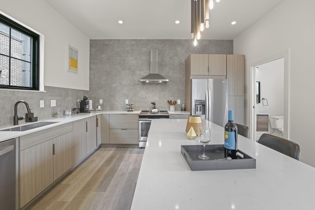 kitchen with stainless steel appliances, sink, wall chimney range hood, light brown cabinets, and light hardwood / wood-style flooring