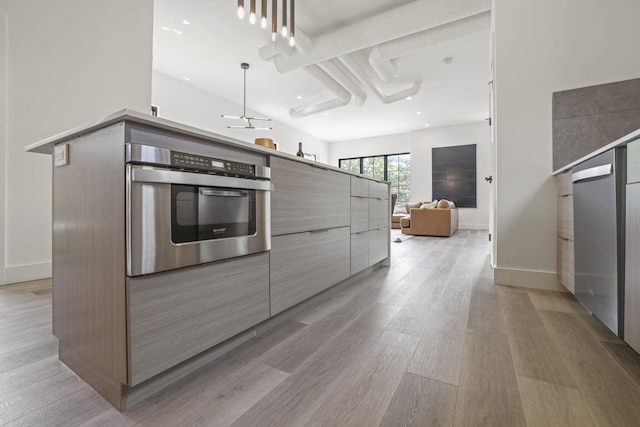 kitchen with ceiling fan, stainless steel oven, decorative light fixtures, and light wood-type flooring