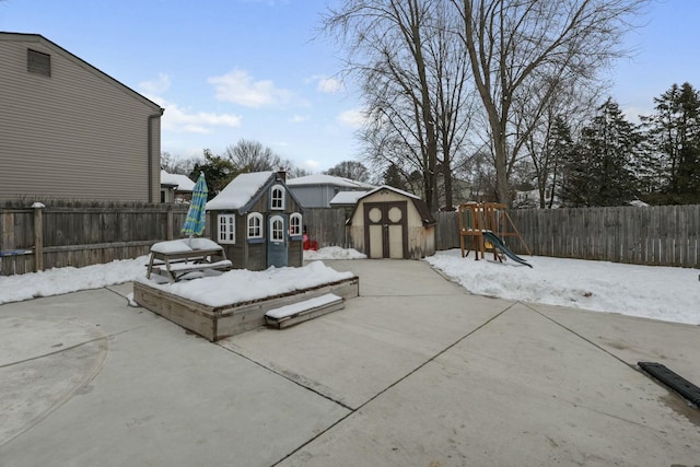 snow covered patio featuring a storage shed and a playground