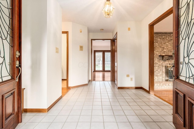 tiled foyer entrance featuring a brick fireplace and an inviting chandelier