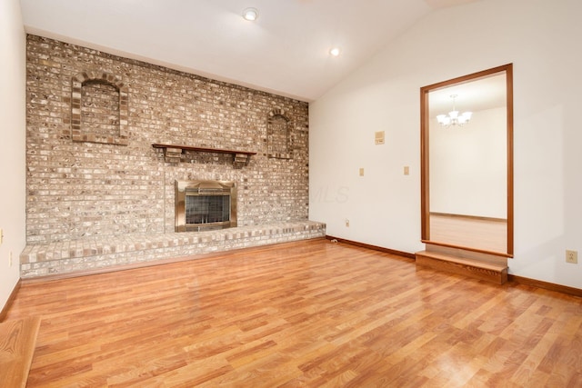 unfurnished living room with hardwood / wood-style floors, a brick fireplace, an inviting chandelier, and lofted ceiling