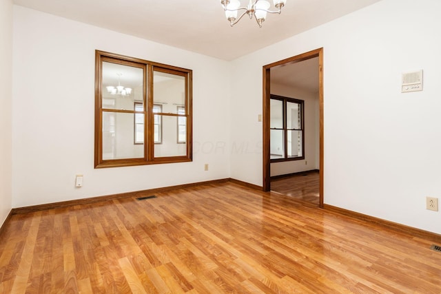 unfurnished room with a wealth of natural light, light wood-type flooring, and an inviting chandelier