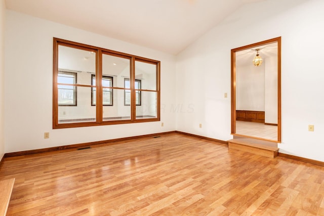 spare room featuring light hardwood / wood-style floors, lofted ceiling, and an inviting chandelier