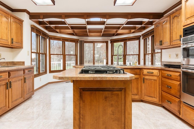 kitchen featuring black gas stovetop, coffered ceiling, double oven, sink, and a center island